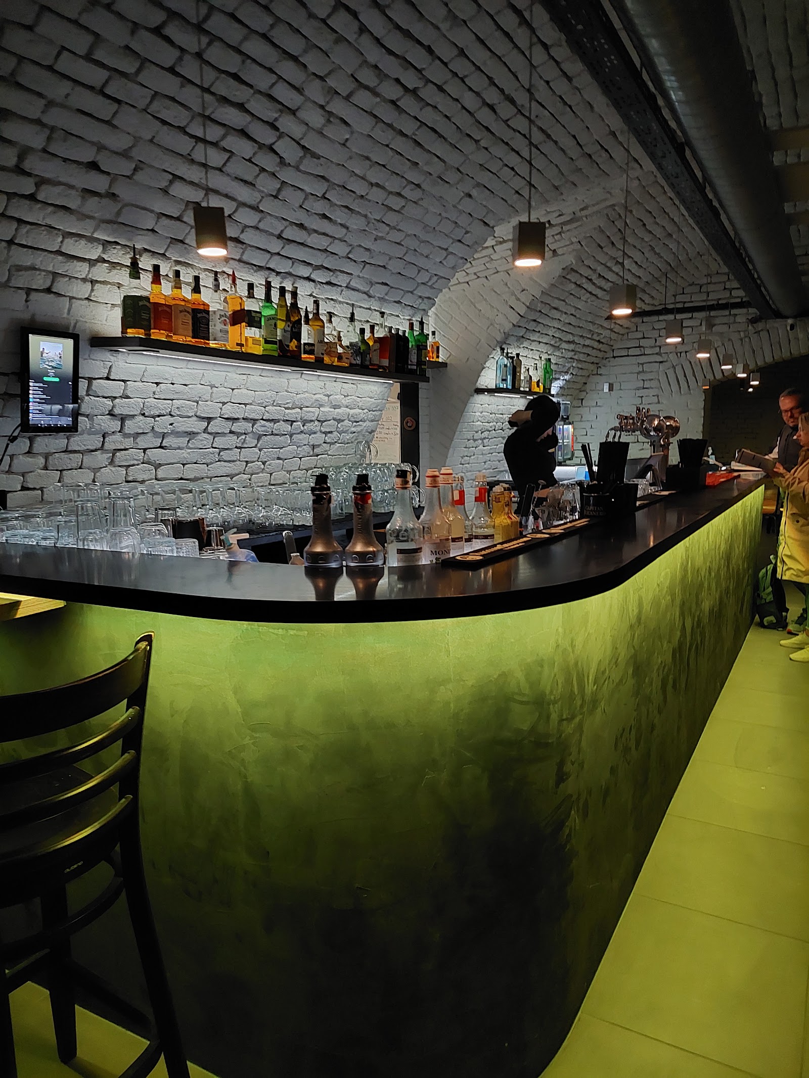 Stylový bar s klenutým stropem a zeleným světlem.